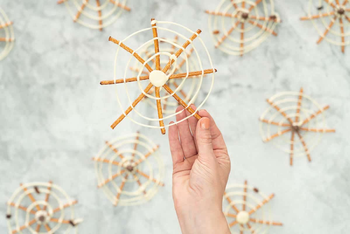 A spider web made from pretzel sticks and white chocolate being held up.
