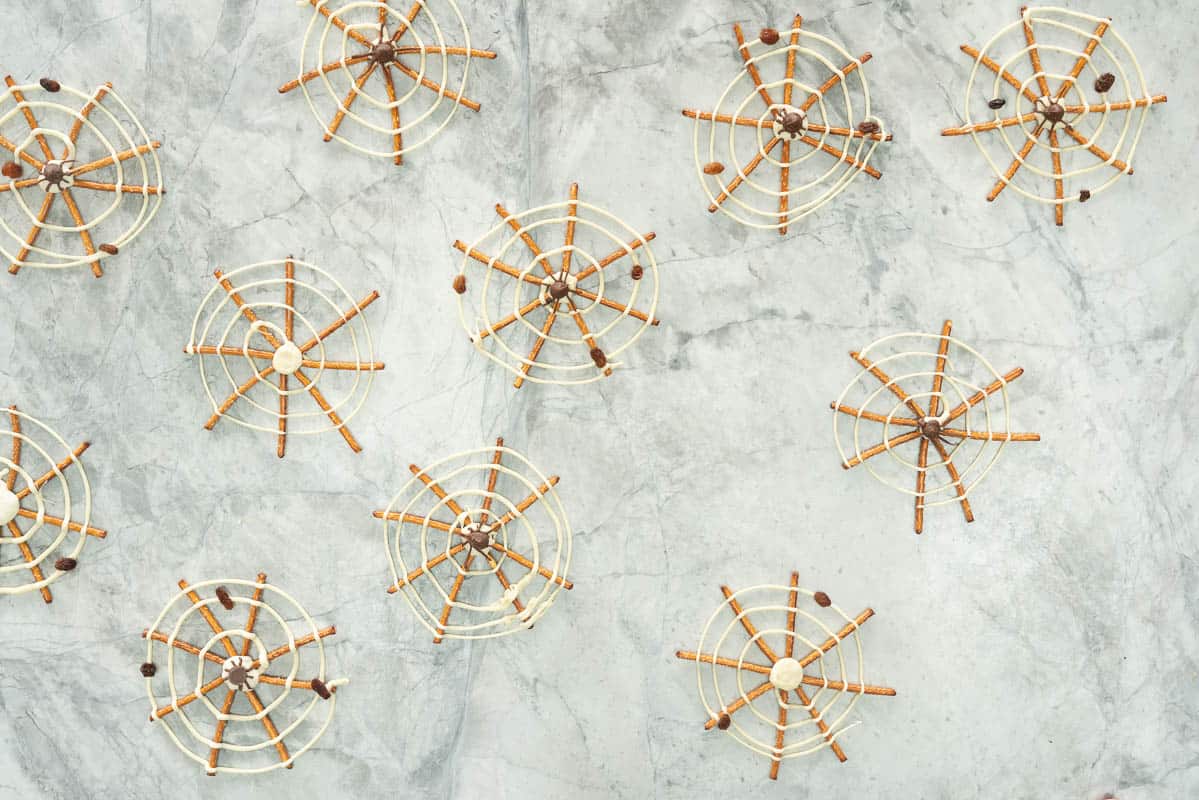 Pretzles decorated to look like spider webs lying on a marble bench top.