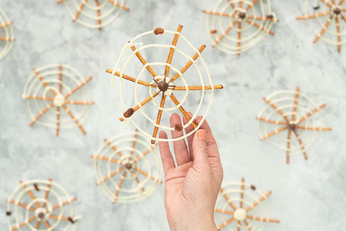 A spider web made from pretzel sticks and white chocolate, and decorated with a milk chocolate spider in the centre being held up.