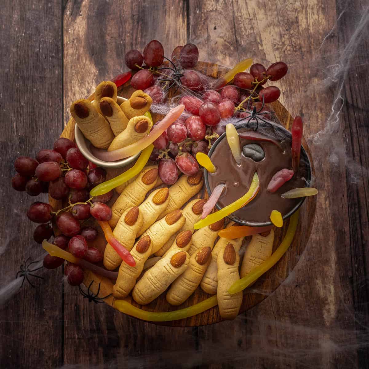 A platter of witch finger cookies and chocolate ganache decorated with gummy snake candy for halloween.