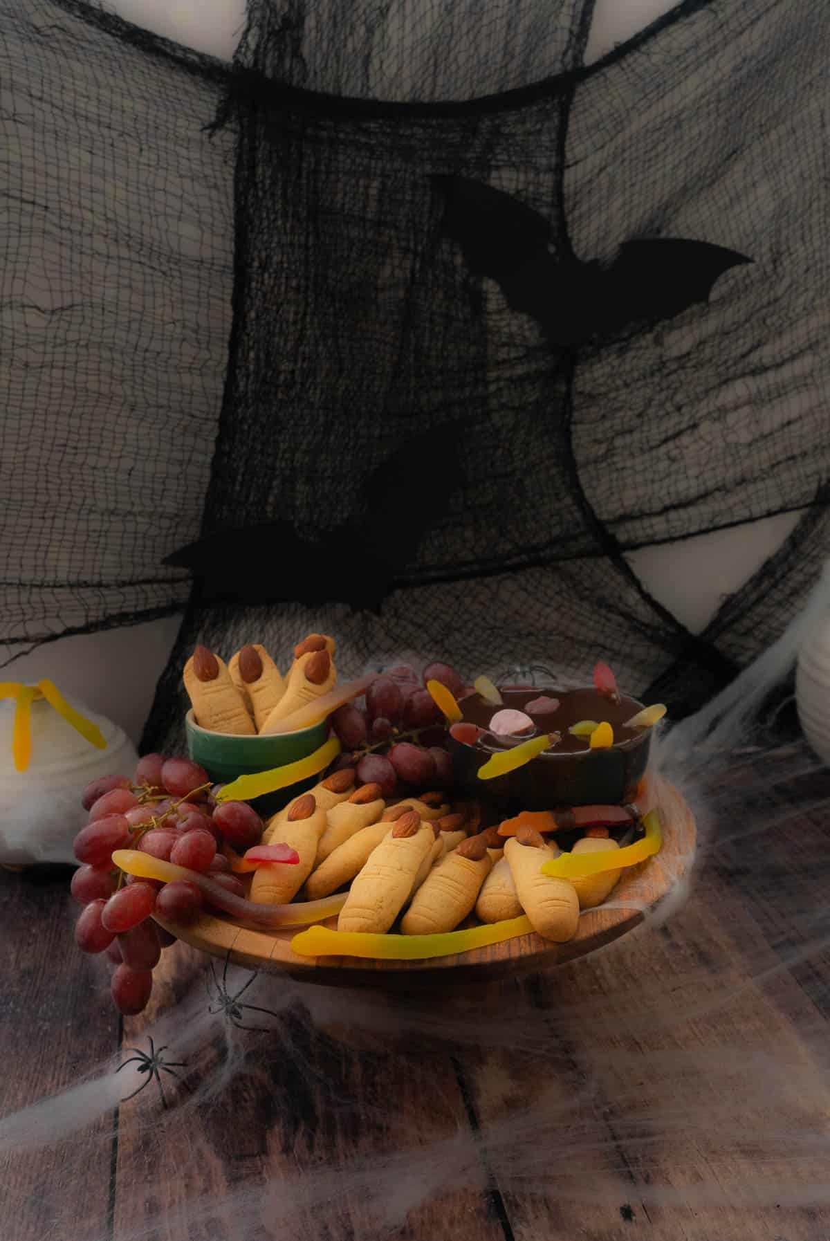 A wooden cake stand decorated for halloween with witch finger cookies and a chocolate witches brew dip