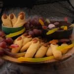 A wooden cake stand decorated for halloween with witch finger cookies and a chocolate witches brew dip
