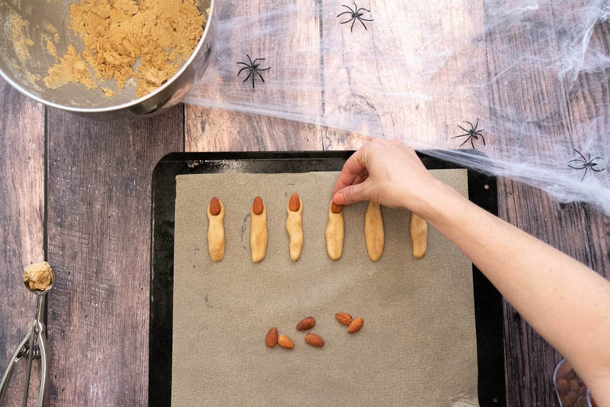 Almonds being pushed into the end of finger cookies to create witch fingernails. 