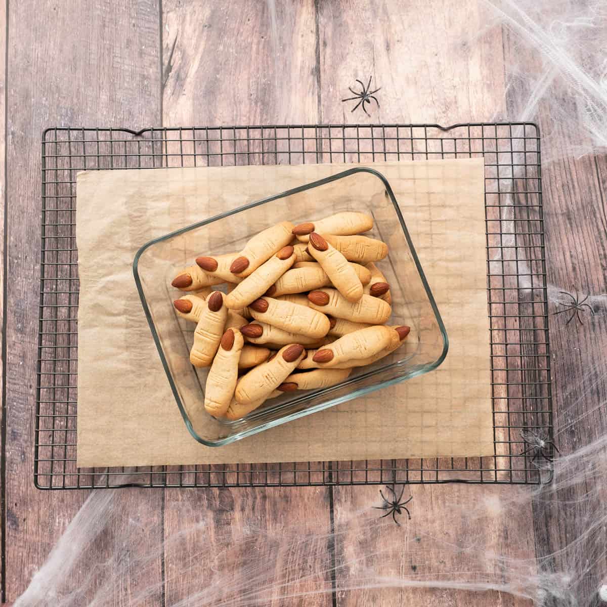 A glass storage conatiner filled with cookies in the shape of witch fingers.