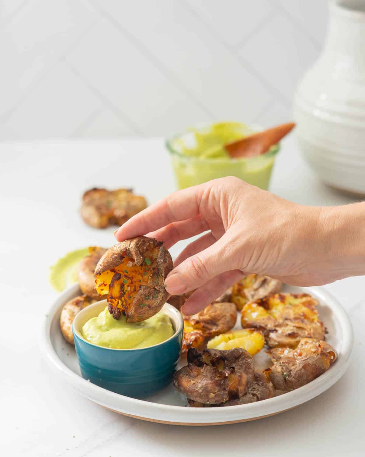 A smashed potato being dipped into a bowl of avocado aioli.