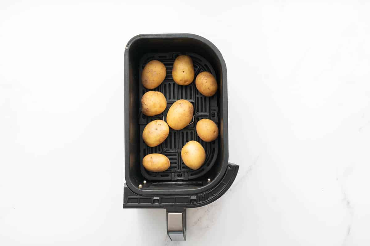 Nine small potatoes in an air fryer basket.