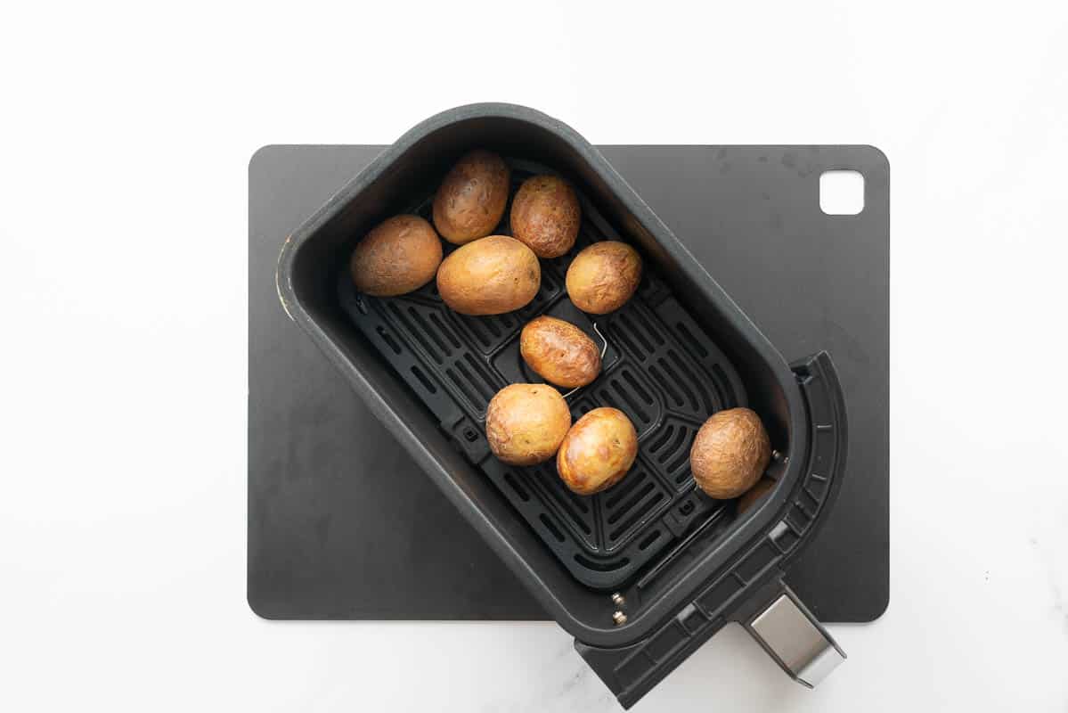 Nine cooked small potatoes in an air fryer basket.