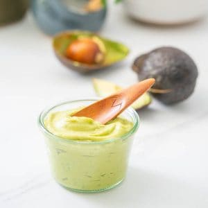 A glass jar filled with creamy avocado with a wooden spoon resting on the surface.