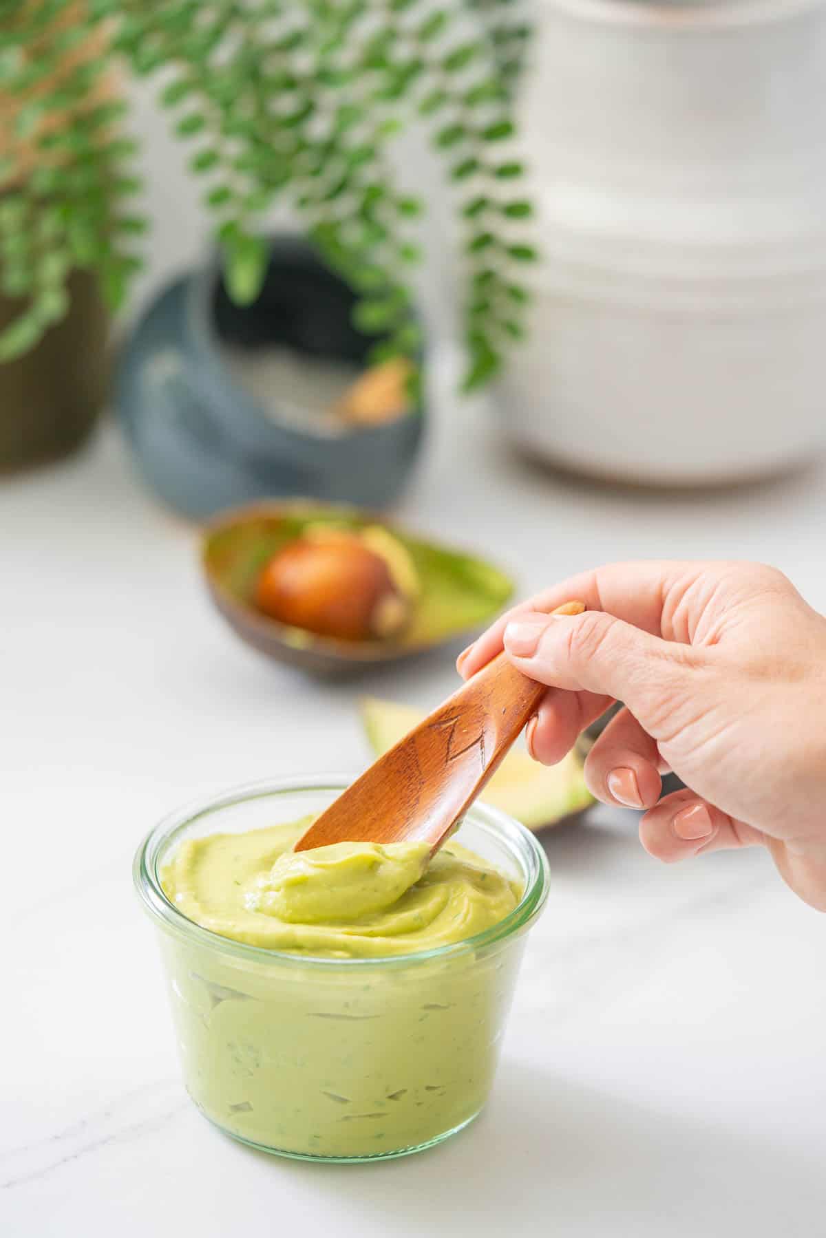 A glass jar filled with creamy avocado being scooped out with a small wooden spoon.