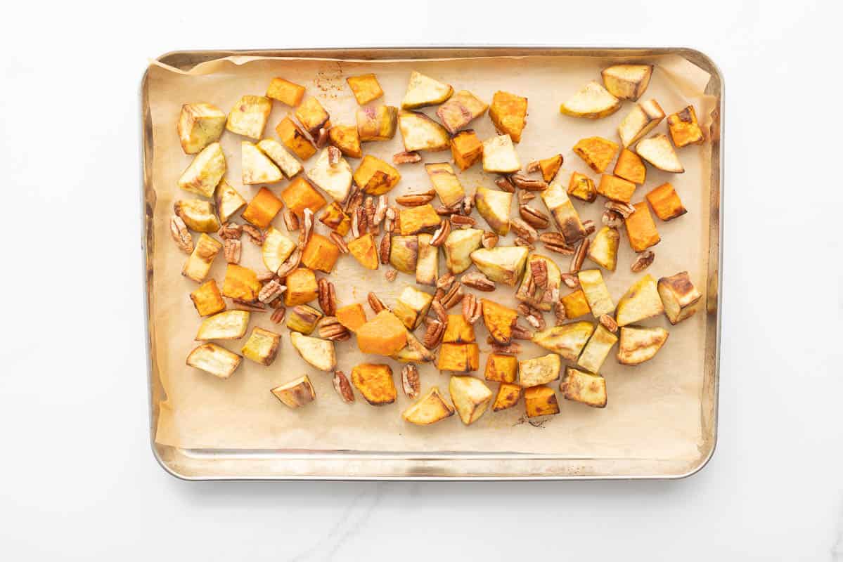 Roasted cubes f orange and gold sweet potato and pecans on a lined baking tray.