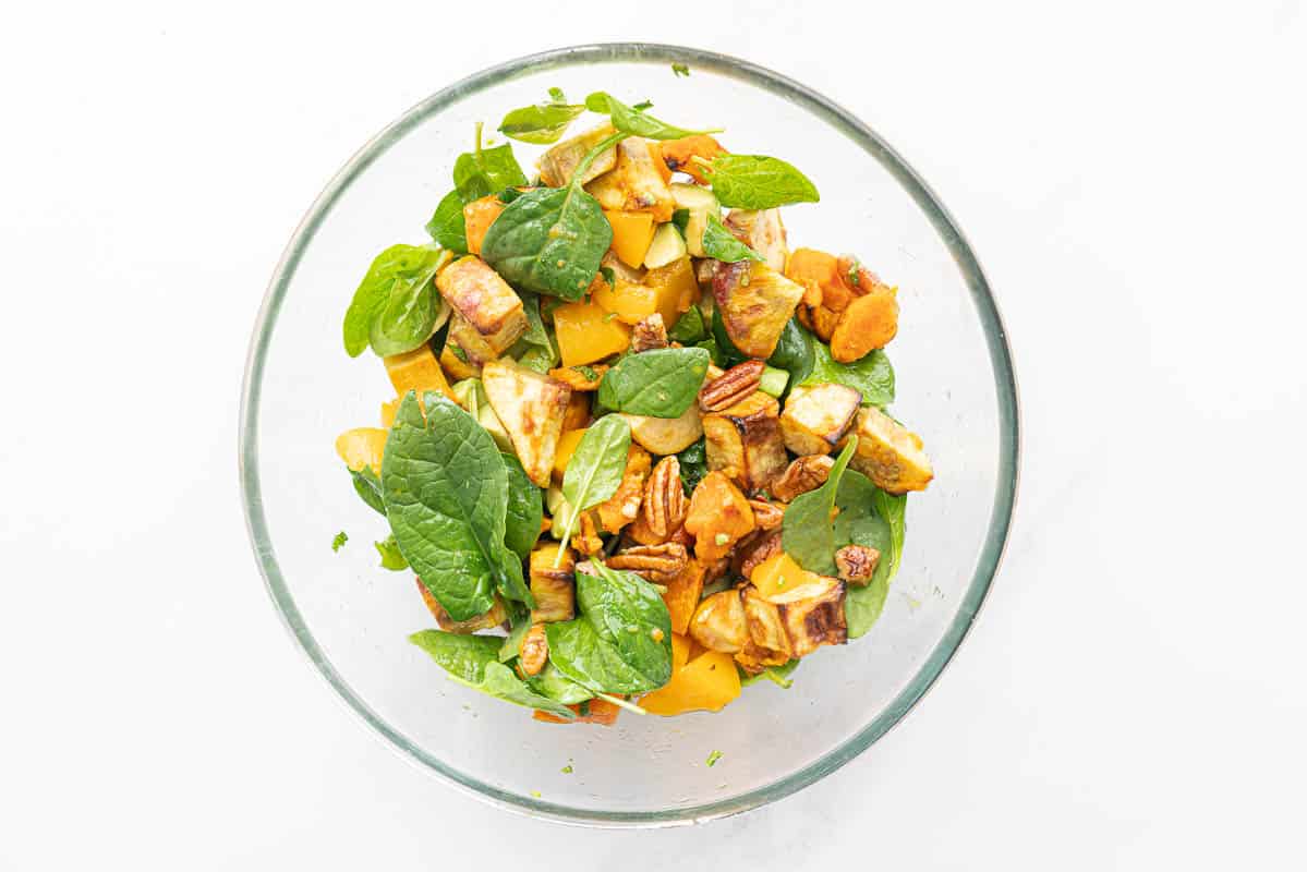 roasted kumara, pecans, avocado, peaches and spinach leaves in a large glass bowl.
