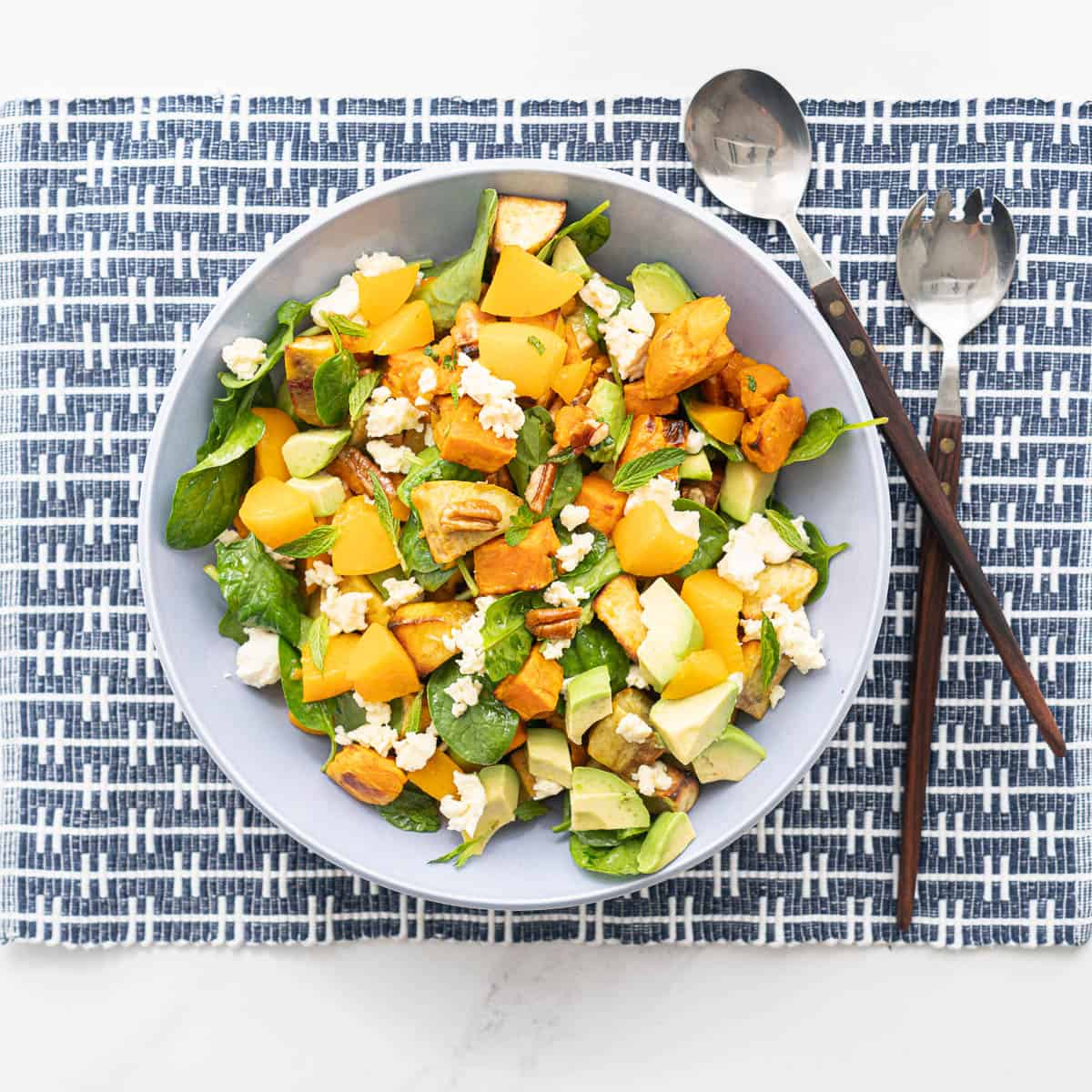 A large blue ceramic bowl of sweet potato and avocado salad on a blue and white woven placemat.