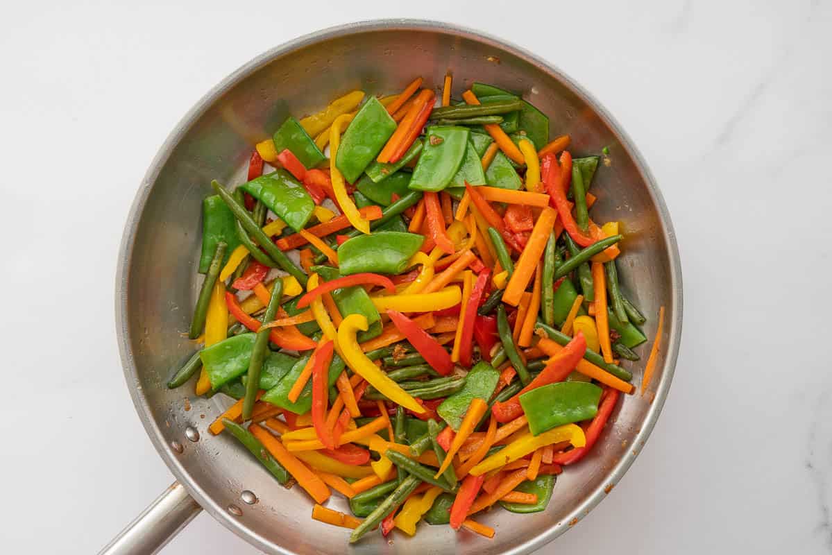 A large stainless steel fry pan of colourful stir fried vegetables.