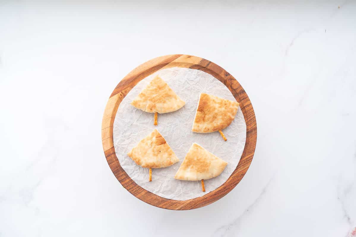 Four triangular pieces of pita bread with a pretzel sric pushed into the base of each piece.