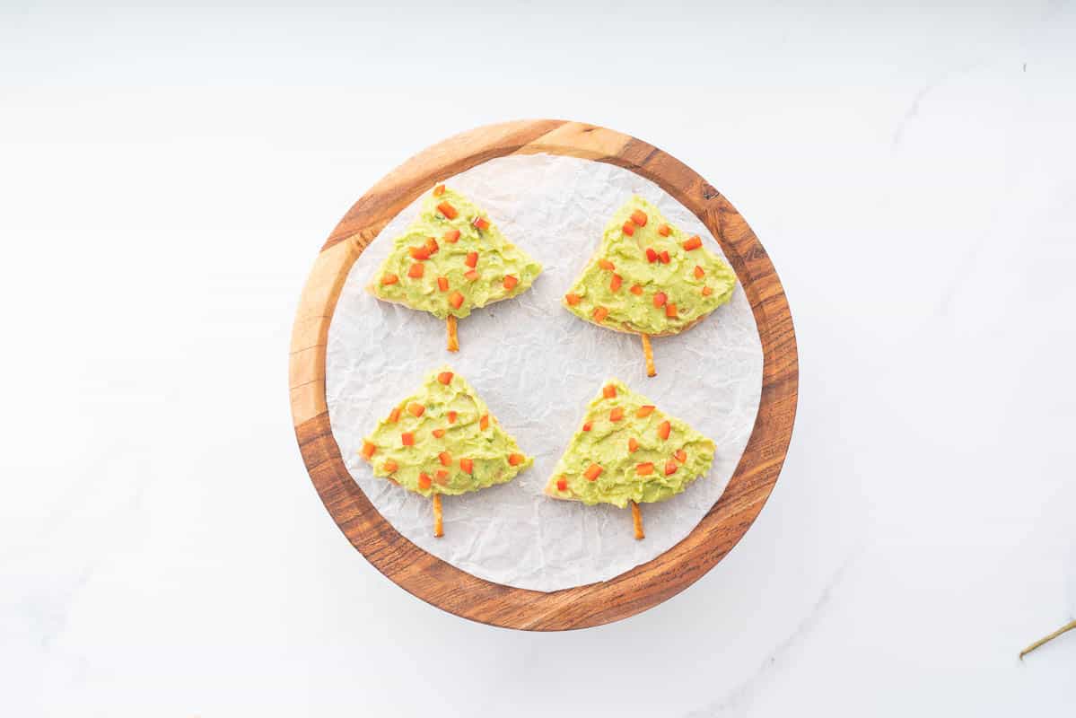 4 triangular pieces of pita bread spread with avocado and sprinkled with small pieces of red capsicum to look like Christmas trees.