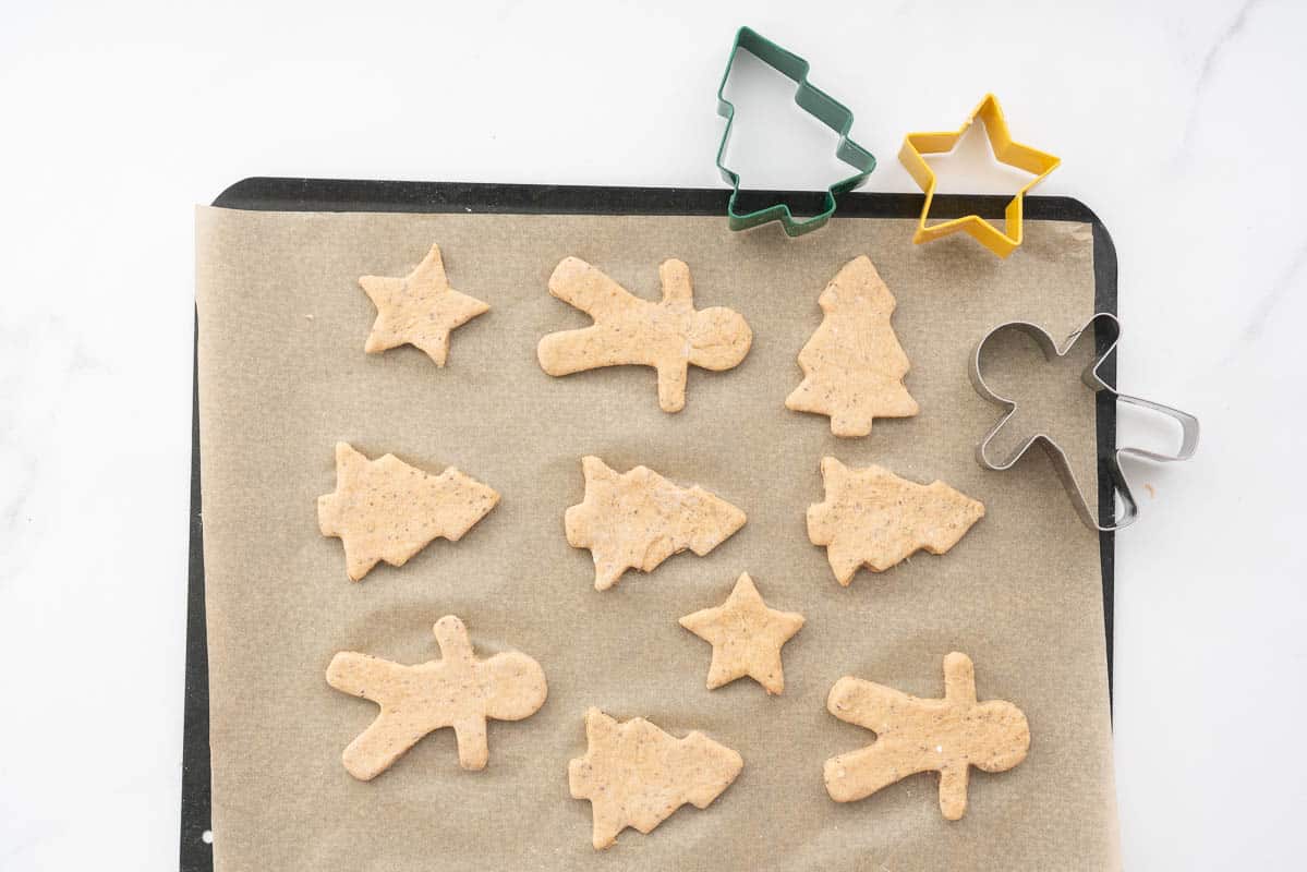 Cookie dough cut in christmas shaped on a lined cookie tray ready to be baked.
