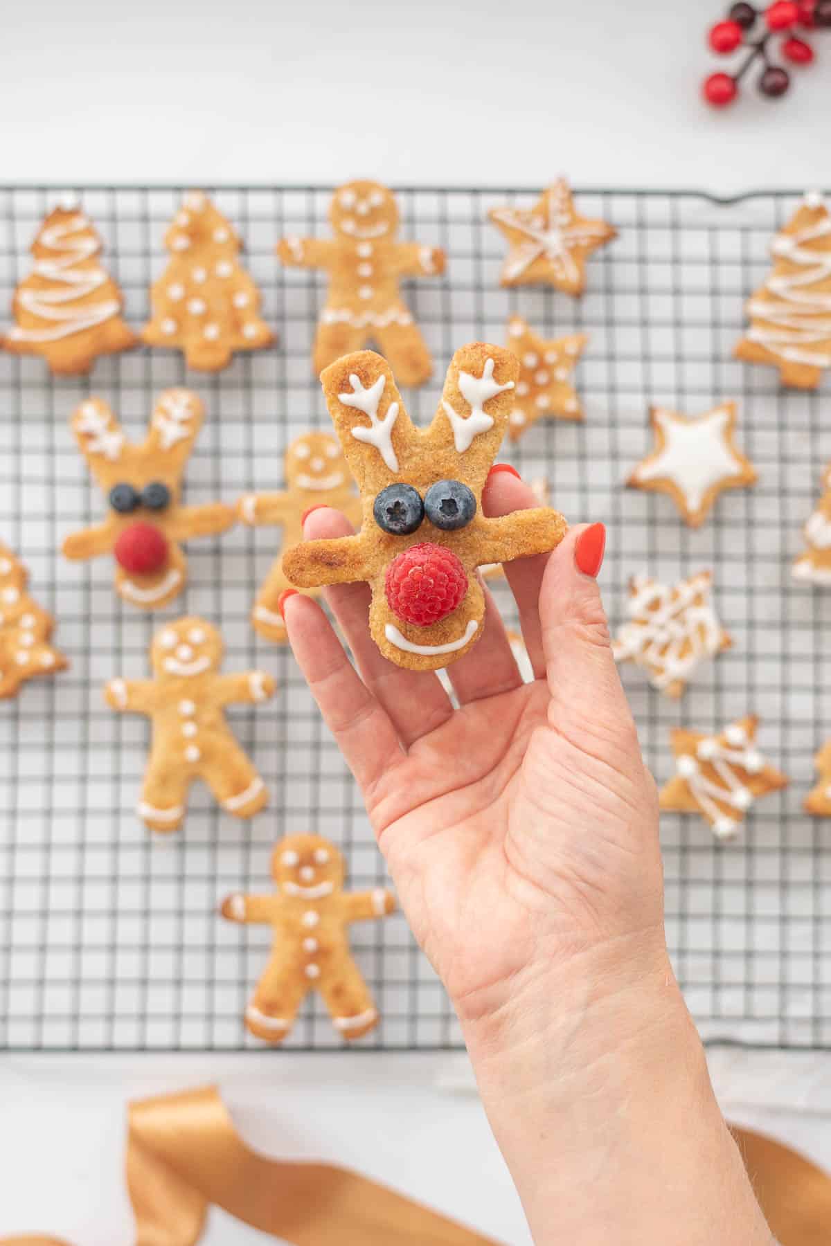 A christmas cookie decorated to look like a reindeer with blueberry eyes and a raspberry nose.
