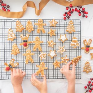 Three children's hand reaching for a christmas cookie cooling on a drying rack.