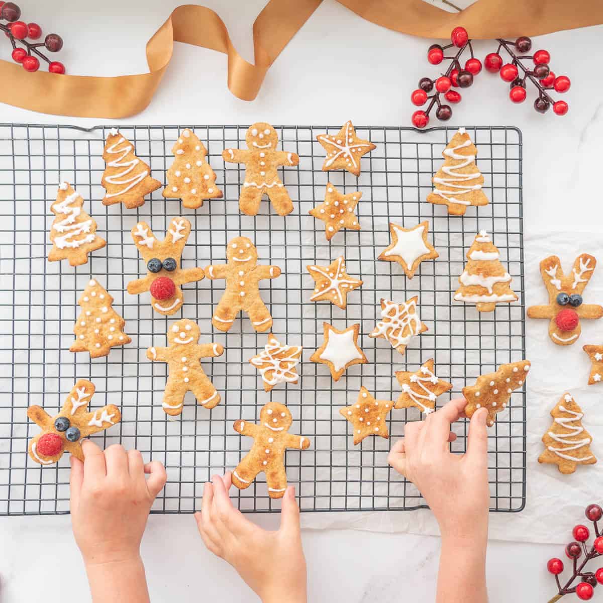 Three children's hand reaching for a christmas cookie cooling on a drying rack.