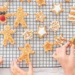Three children's hand reaching for a christmas cookie cooling on a cooling rack.