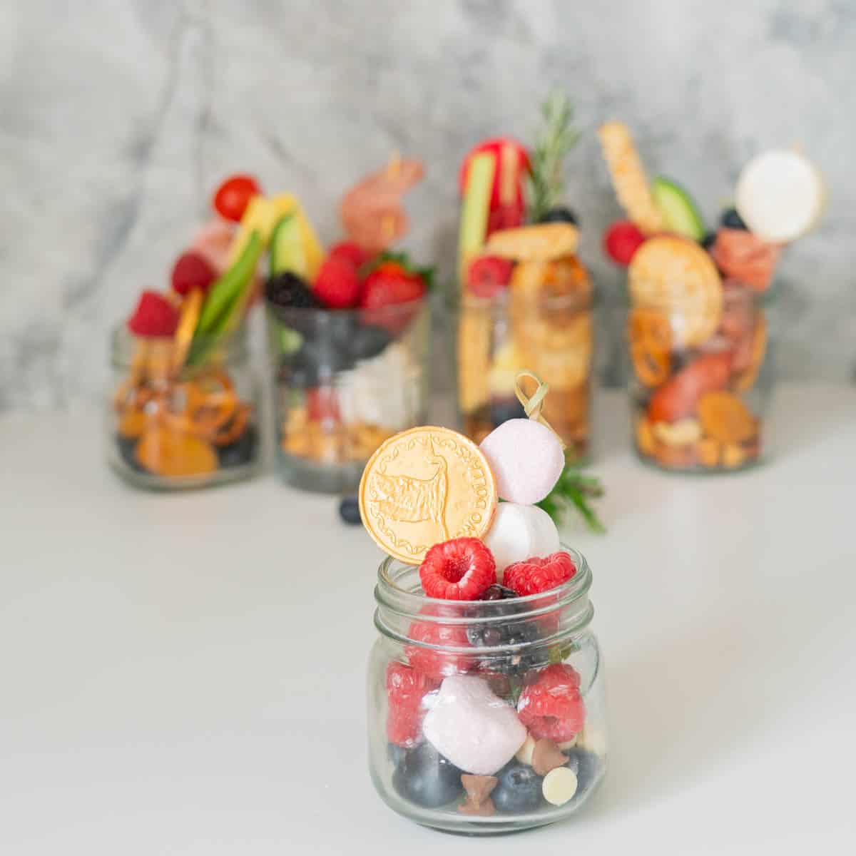 A small jar filled with berries, marshmallows and chocolate coins.