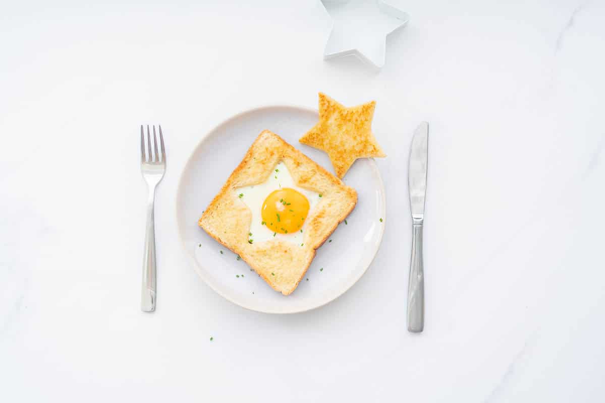 An egg cooked into the star shaped hole of a piece of toast on a plate with a golden star piece of toast to the side.