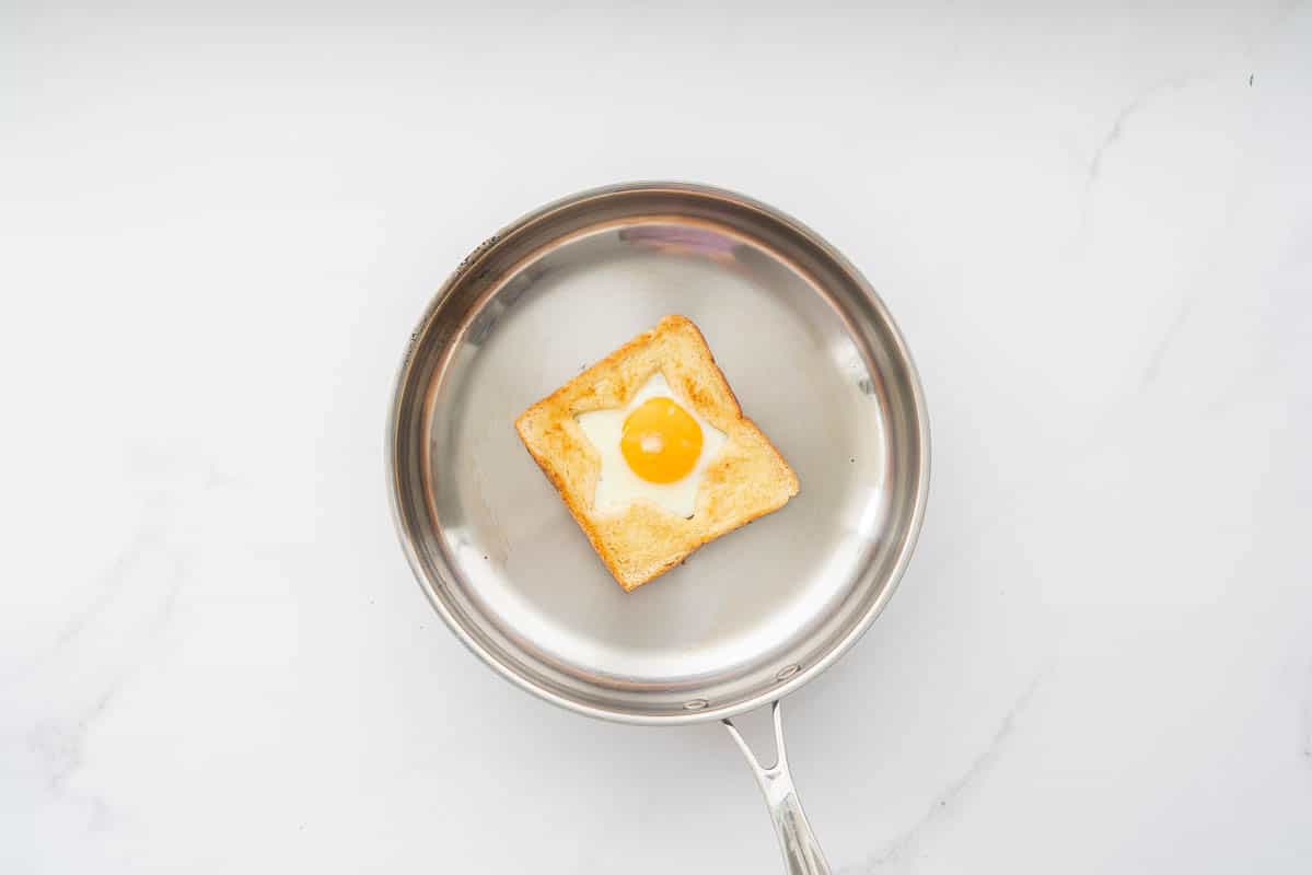 An egg cooked into the star shaped hole of a piece of toast in a fry pan.