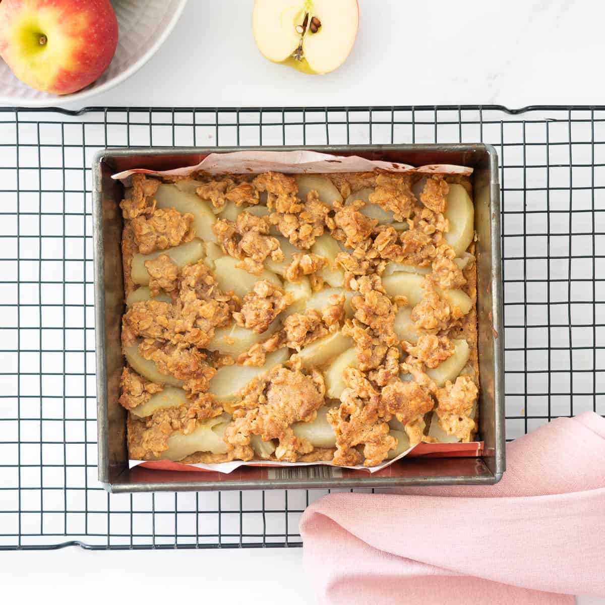 Apple slice in a cake tin on a cooling rack.