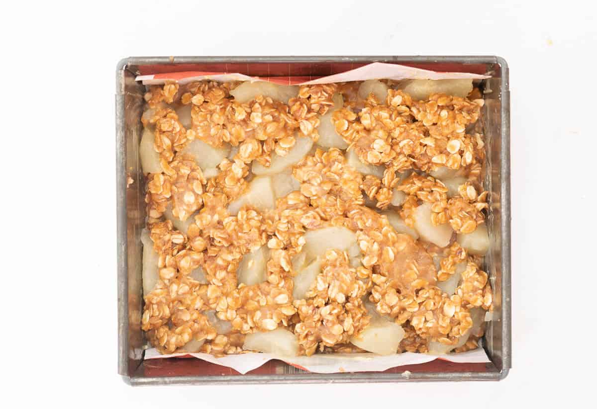 Apple slices topped with an oat crumble topping in a lined slice tin.