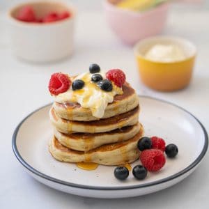 Four thick pancakes stacked on a tower topped with yoghurt, berries and yoghurt.