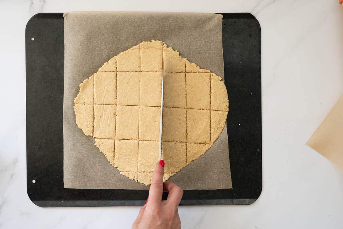 Cracker dough beeing scored into rectangular shapes with a knife. 