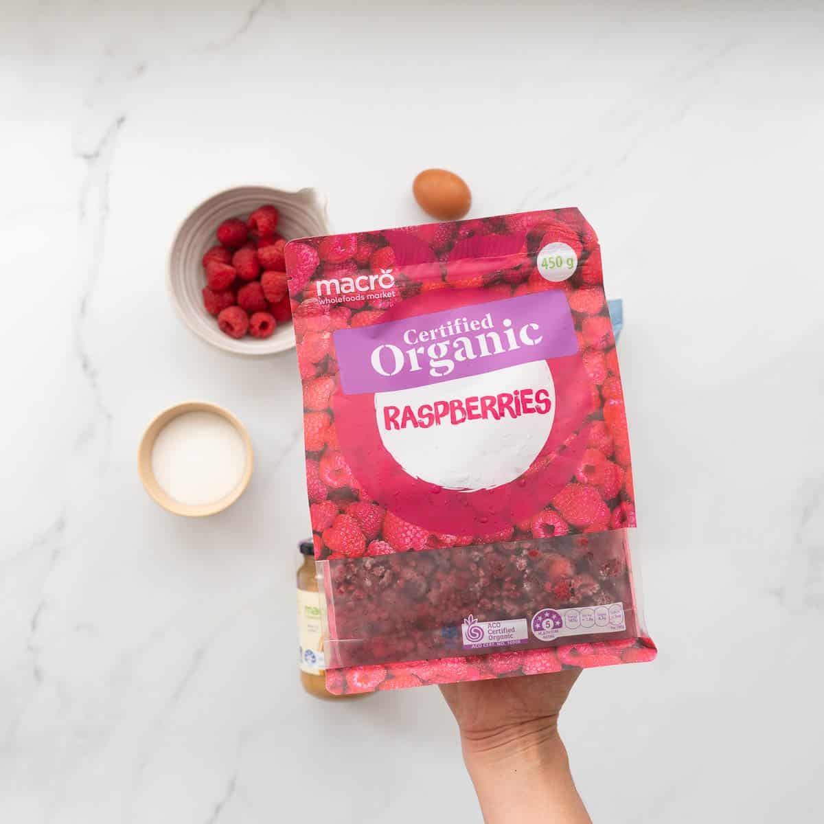 A bag of macro organic frozen raspberries being held above a marble bench.