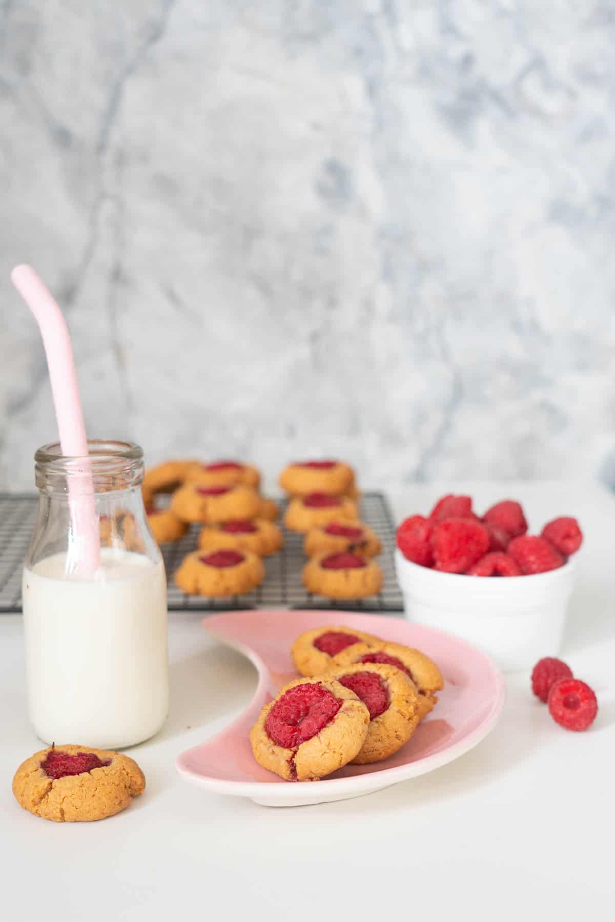 Raspberry thumbprint cookies on a pink plate with a small bottle of milk with a straw.