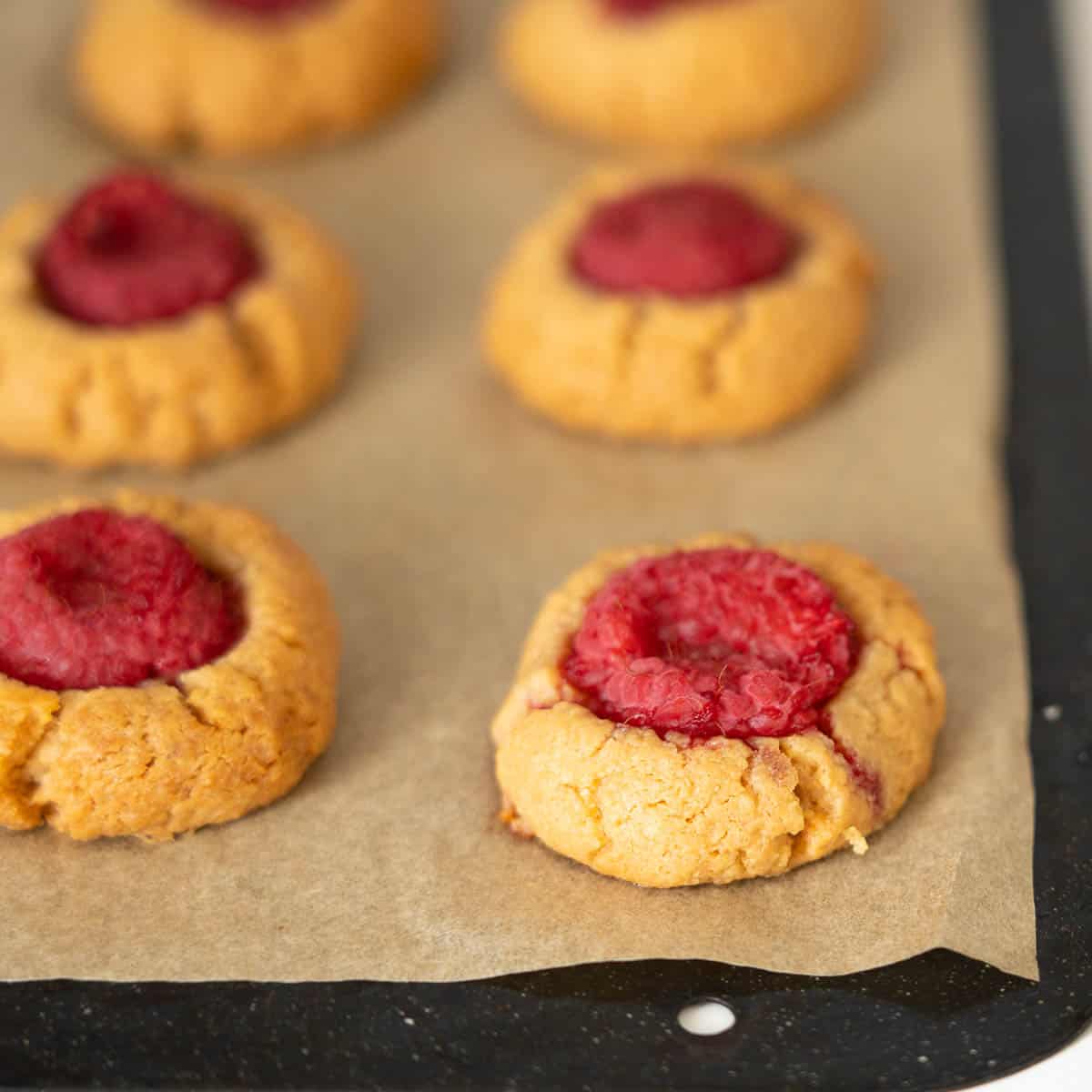 Raspberry thumbprint cookies on a baking paper lines tray.