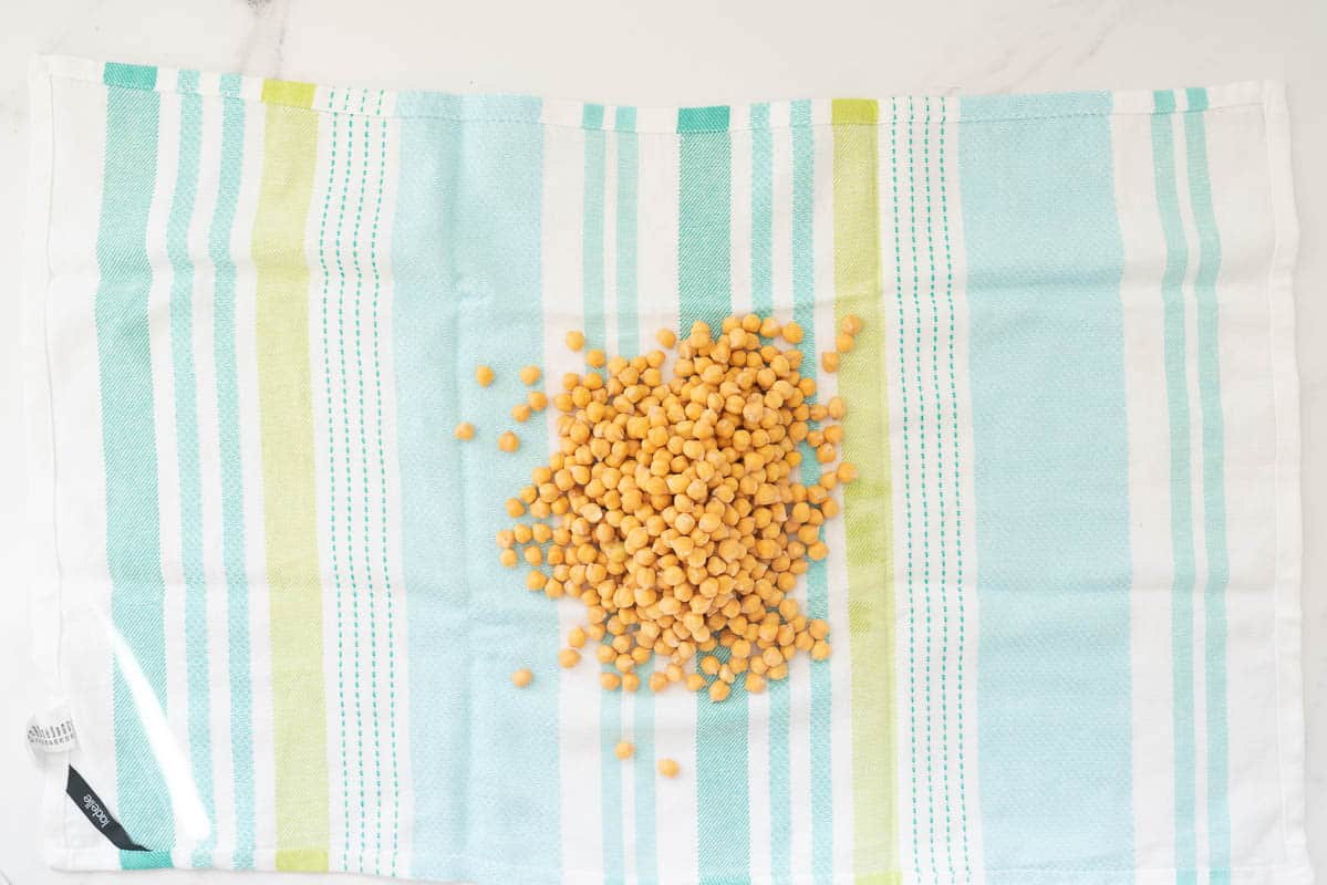 Soaked chickpeas being dried in a green and blue striped tea towel. 