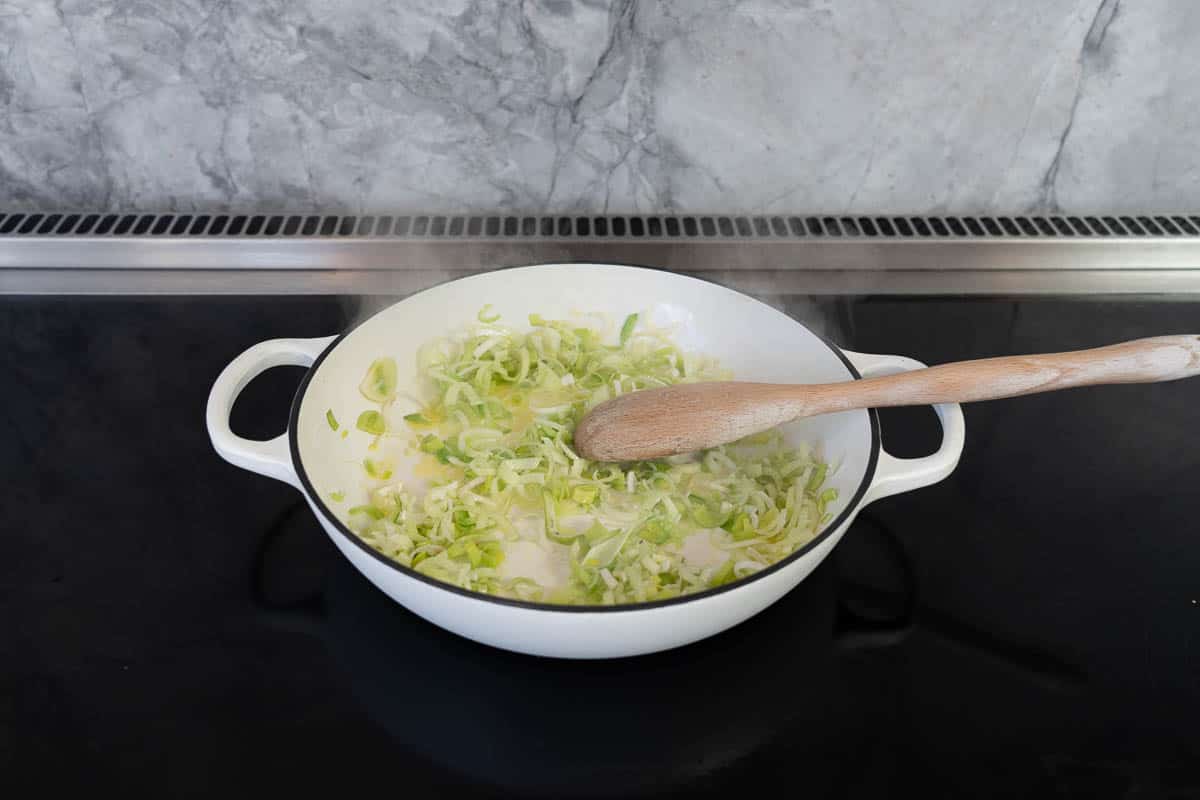 Sliced leek in a large white casserole dish on a stove top.