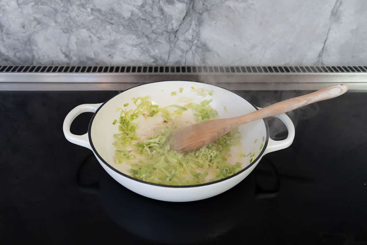 Sautéed sliced leek in a large white casserole dish on a stove top.