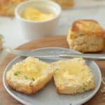 A close up of a buttered scone on a grey ceramic plate.