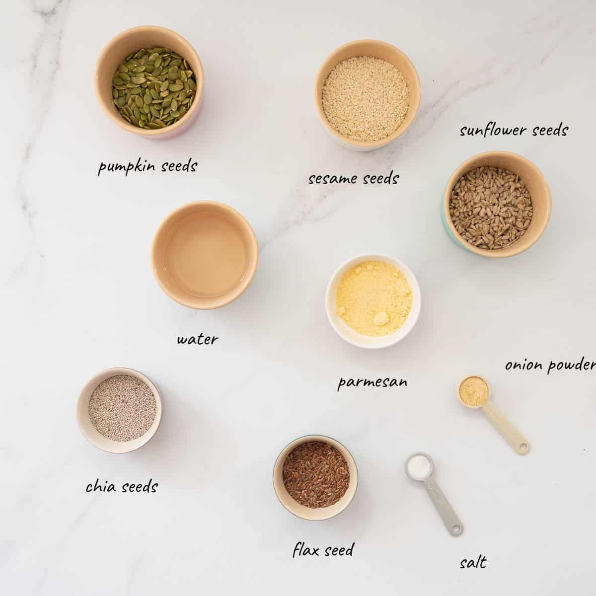 The ingredients to make seed crackers laid out on a bench top with text overlay. 