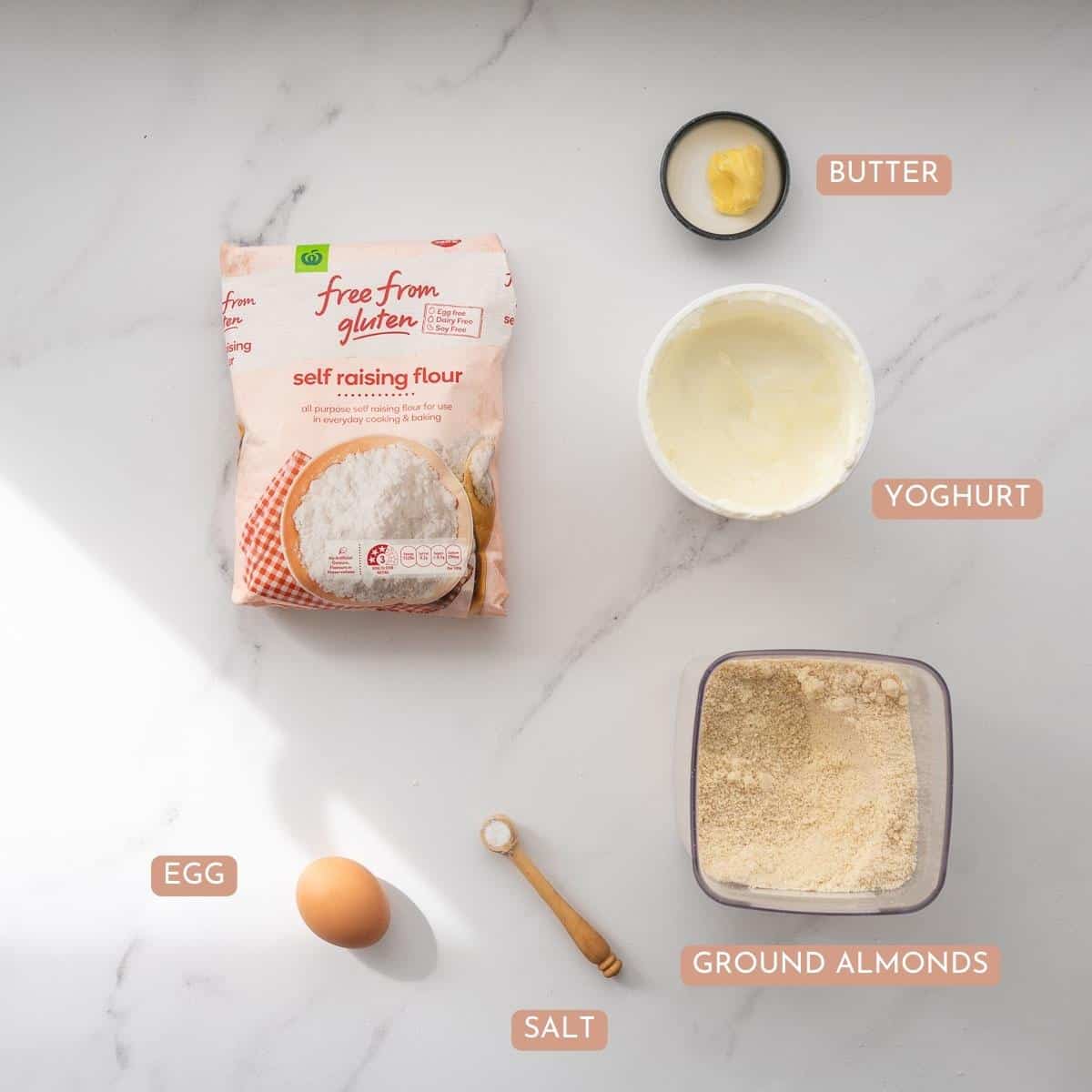 The ingredients to make gluten free bunny buns laid out on a bench top with text overlay labels.