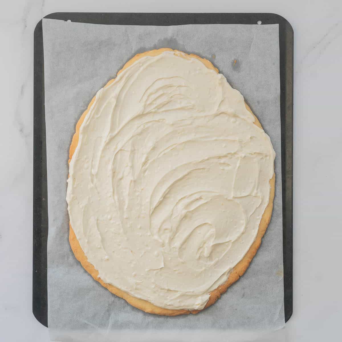 Cream cheese frosting spread over a large egg shaped pizza base sized cookie. 
