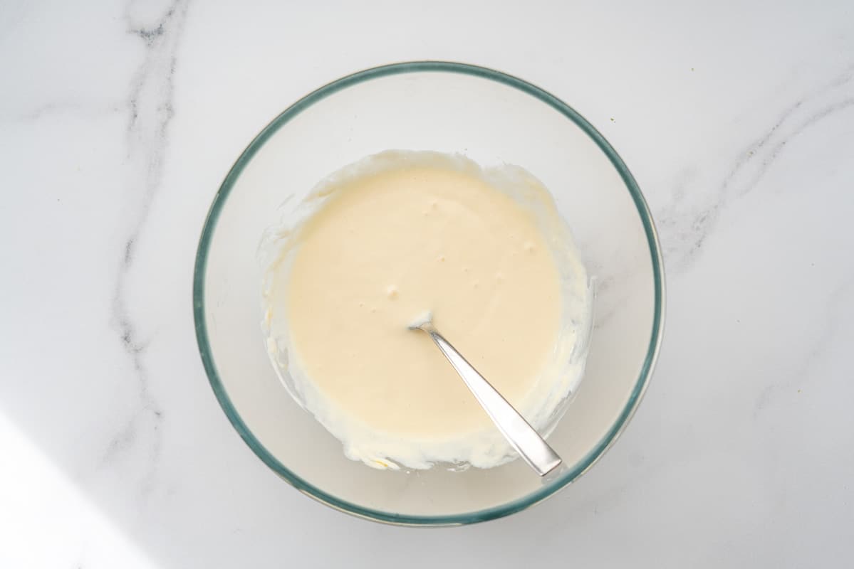 A glass mixing bowl of egg and yoghurt mixed together with a fork.
