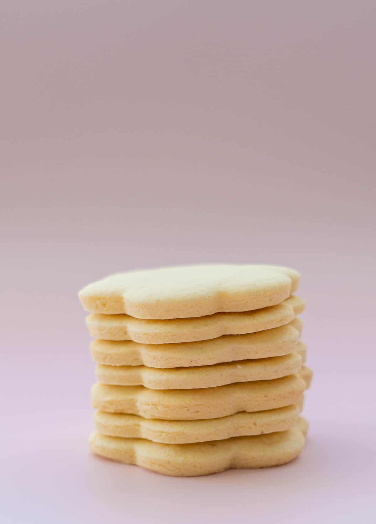 A tower of seven flower shaped cookies on a pink background