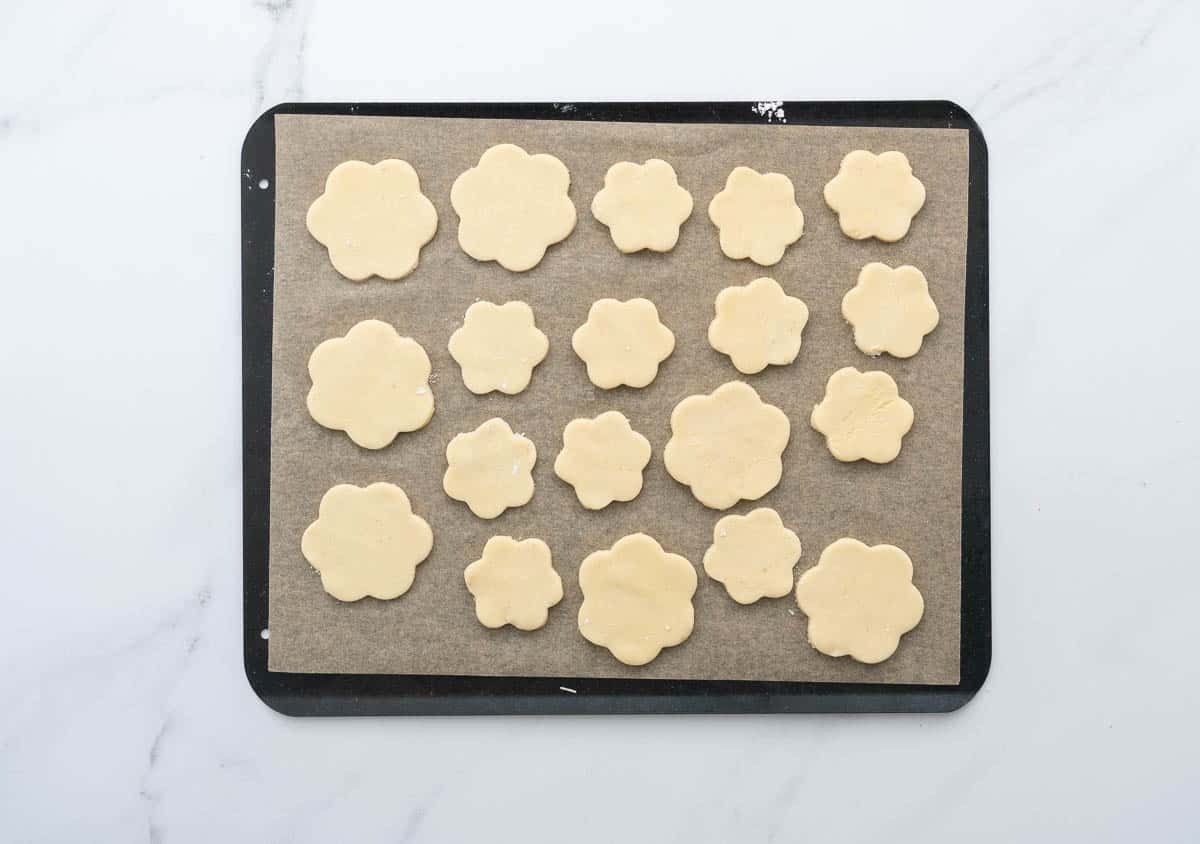 Cookies cut into flower shapes sitting on a lined cookie sheet ready to go into the oven. 