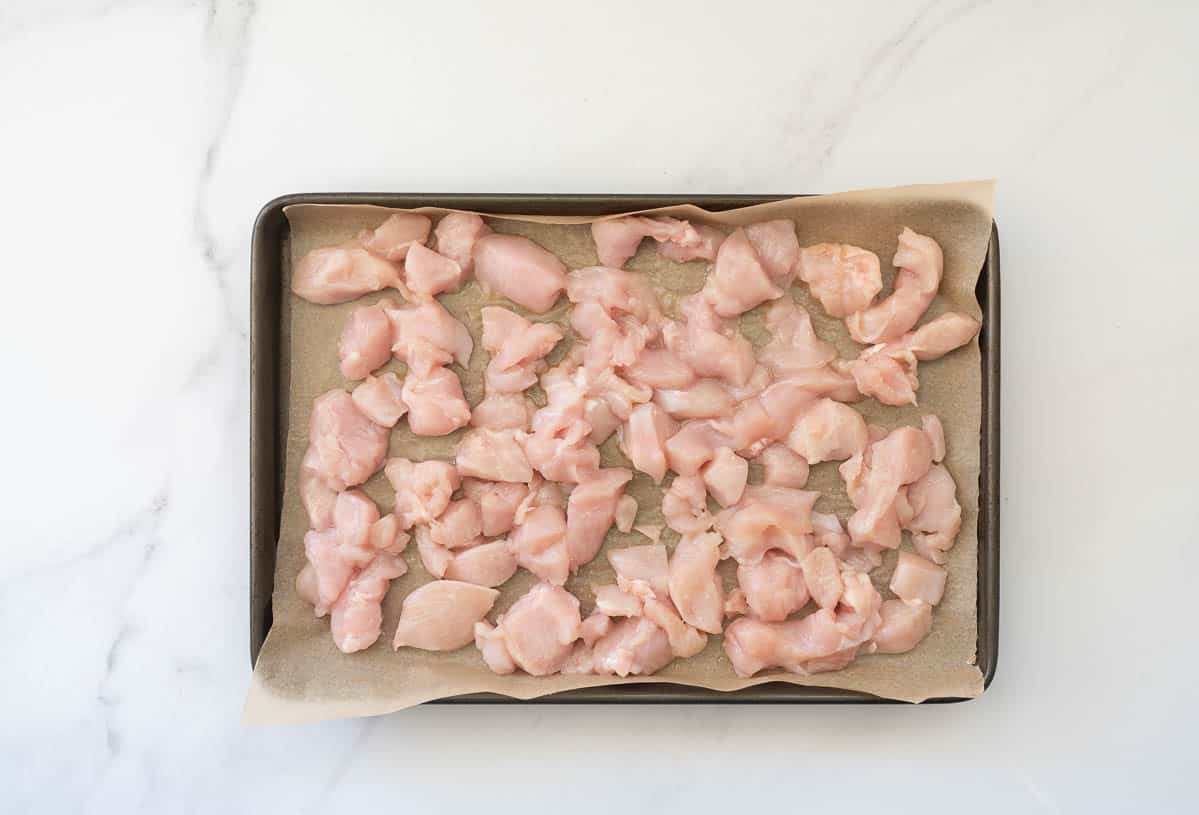 Diced chicken breast laid out on a lined baking tray.