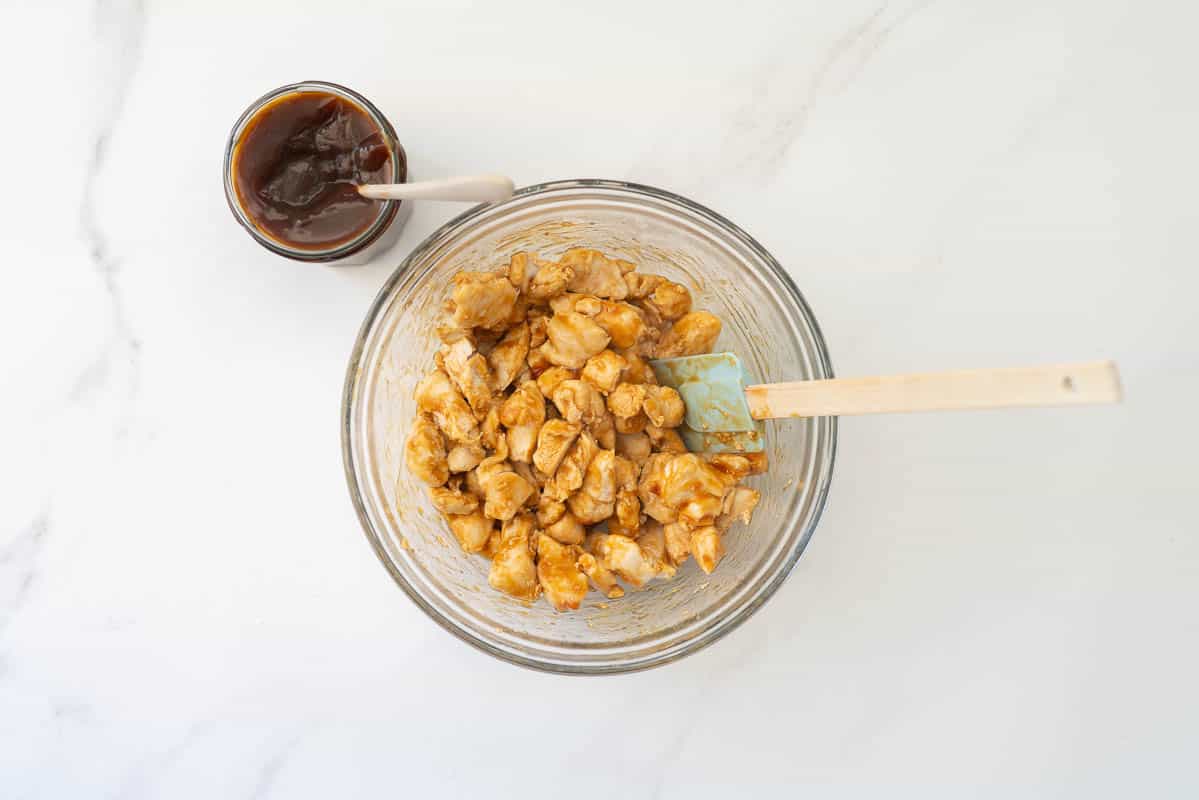 Cooked diced chicken coated in teriyaki sauce in a large glass bowl.