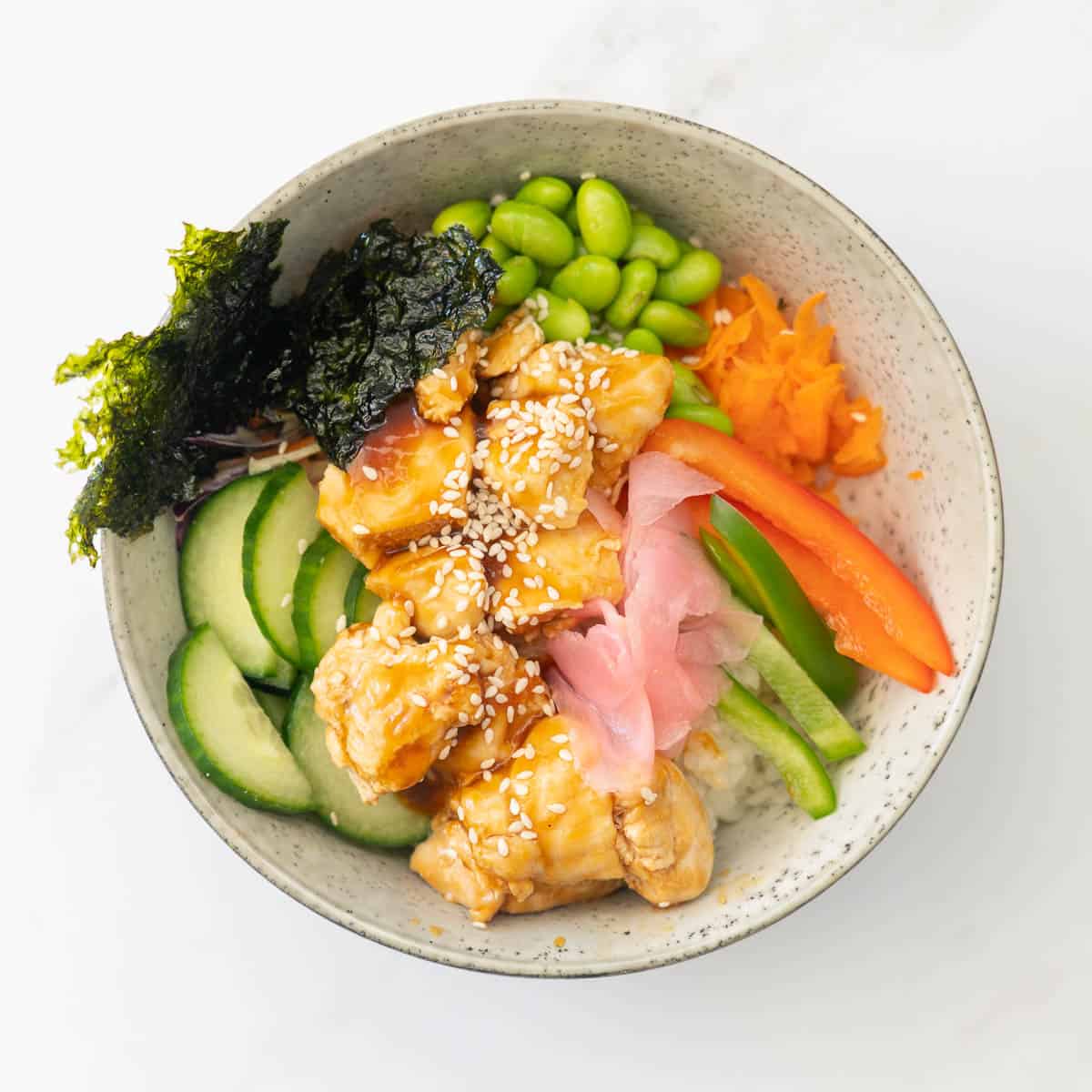 A bowl of teriyaki chicken Rice, vegetables and toasted seaweed pickled ginger and sesame seeds.