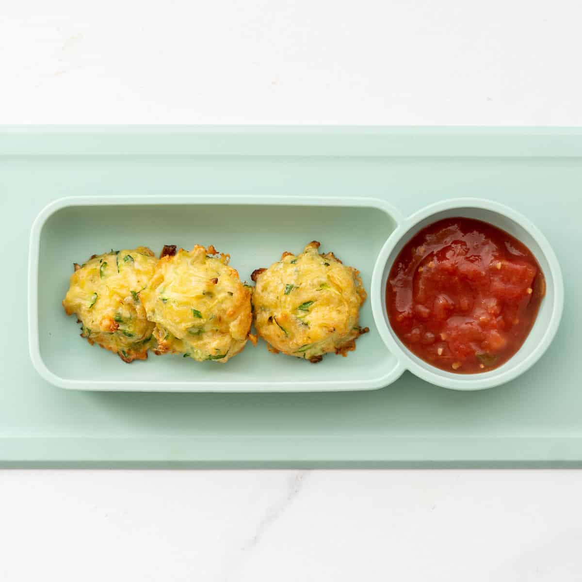 Three zucchini tots on a silicon feeding tray with tomato salsa.