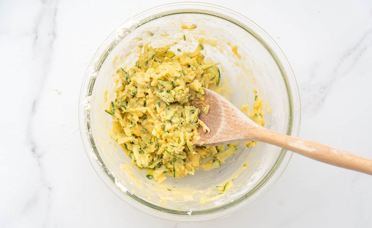 zucchini tot batter in a glass mixing bowl with a wooden spoon.