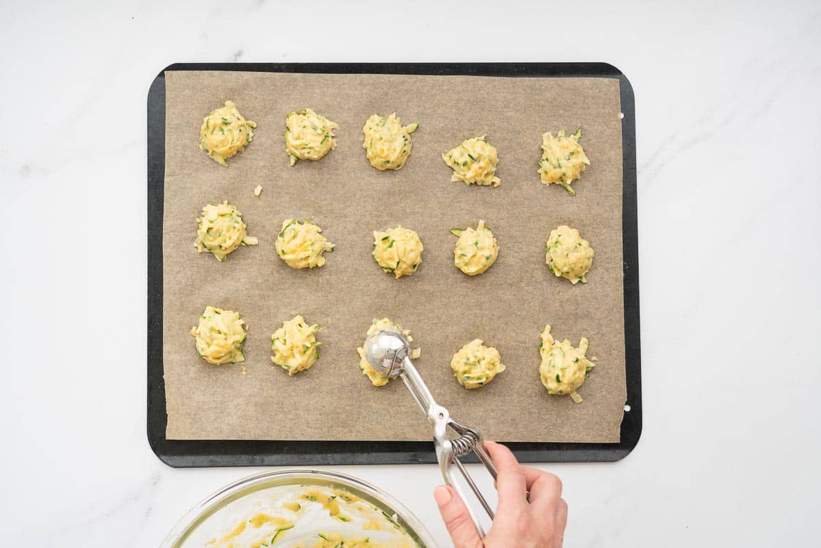 15 scoops of zucchini batter on a lined baking tray.